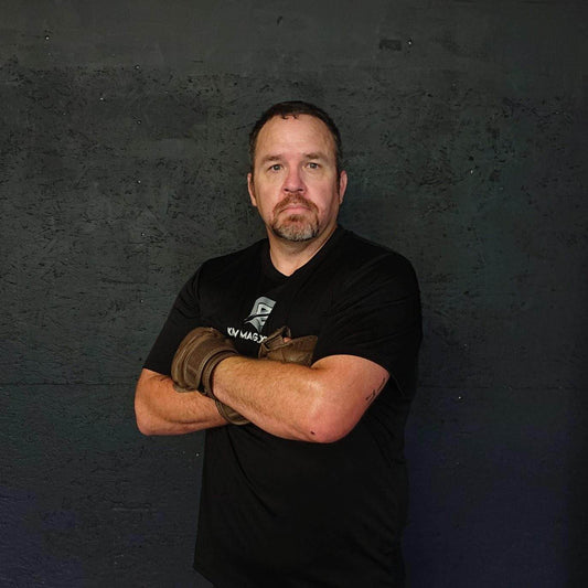 Mikey at Krav Maga posing with his arms crossed after a long workout, wearing a black krav shirt and mma style gloves.